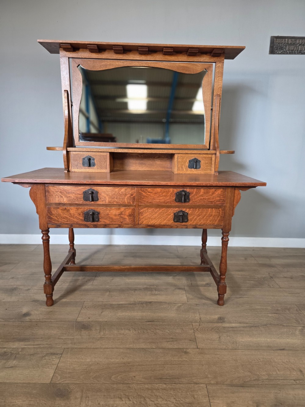 An Arts and Crafts solid oak dressing table featuring an upper mirror superstructure with side trinket drawers above a lower four-drawer chest with dark metal handles.
