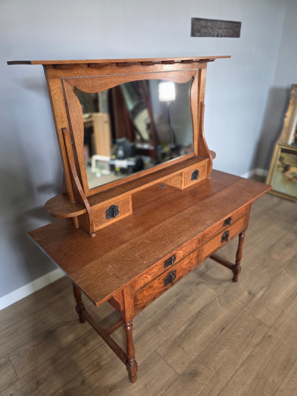 An Arts and Crafts solid oak dressing table featuring an upper mirror superstructure with side trinket drawers above a lower four-drawer chest with dark metal handles. View IV