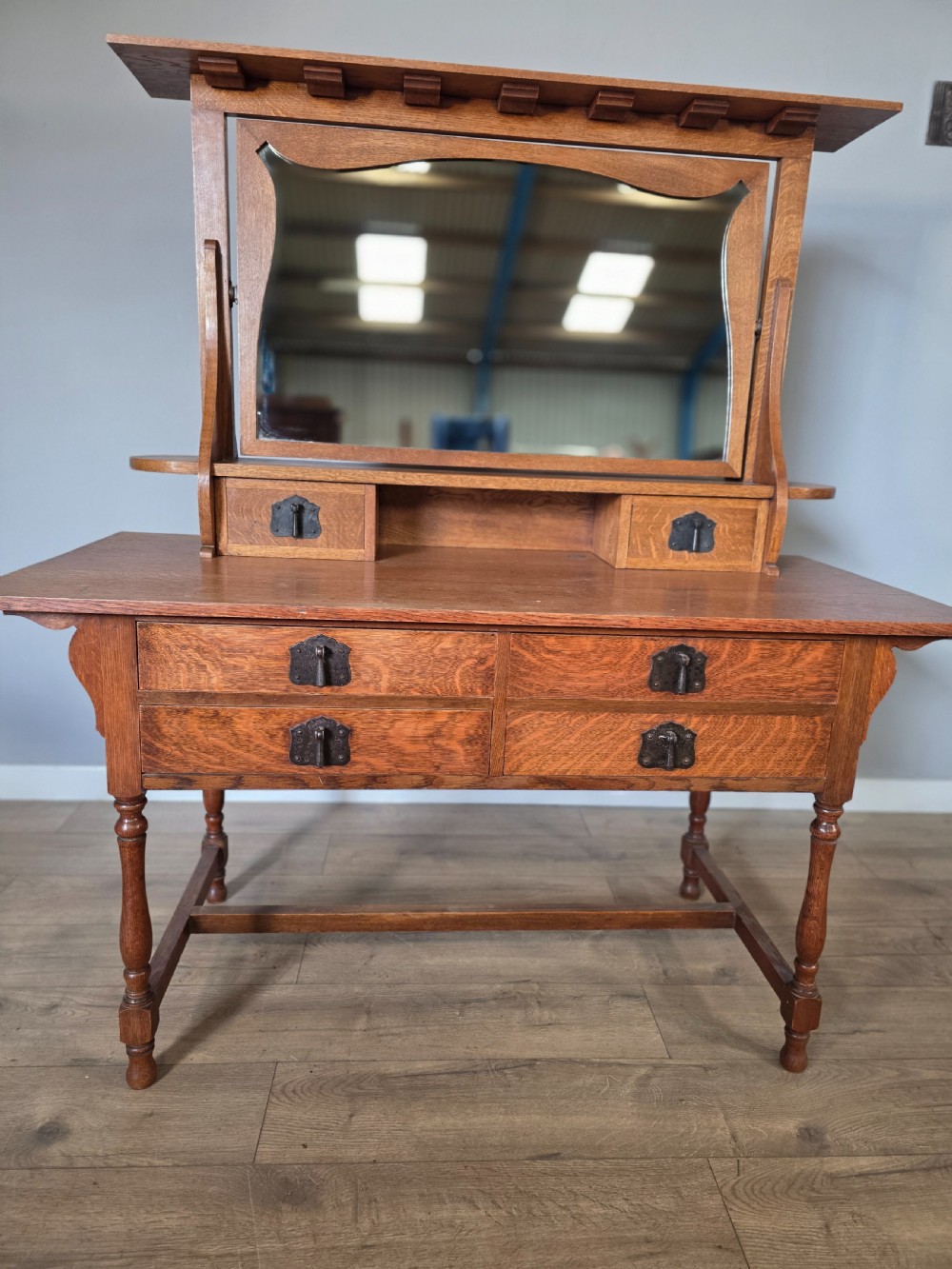 An Arts and Crafts solid oak dressing table featuring an upper mirror superstructure with side trinket drawers above a lower four-drawer chest with dark metal handles. View V