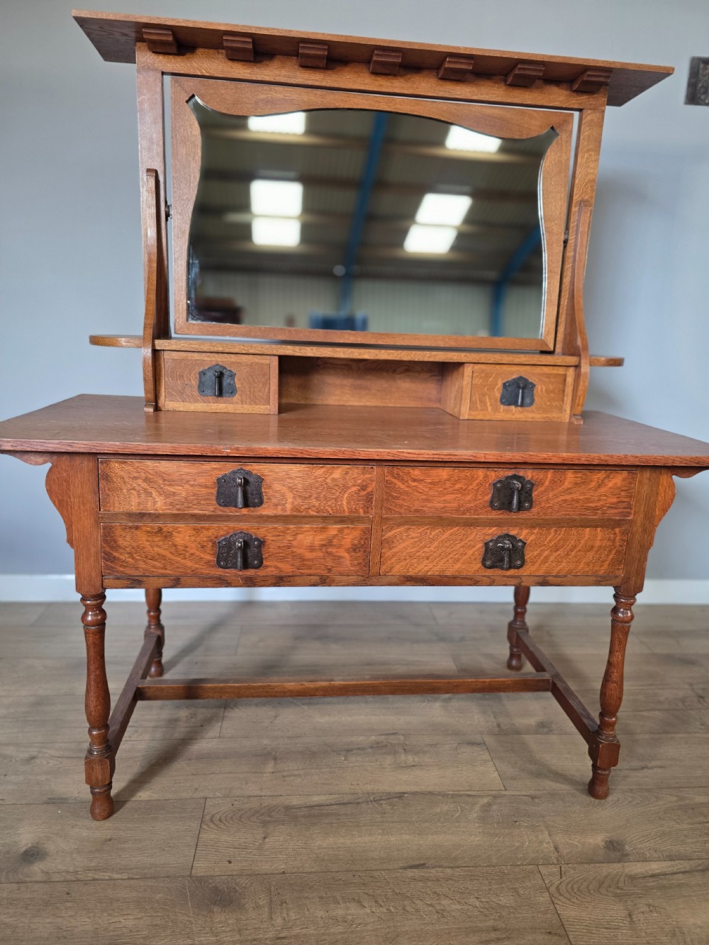An Arts and Crafts solid oak dressing table featuring an upper mirror superstructure with side trinket drawers above a lower four-drawer chest with dark metal handles. View VI