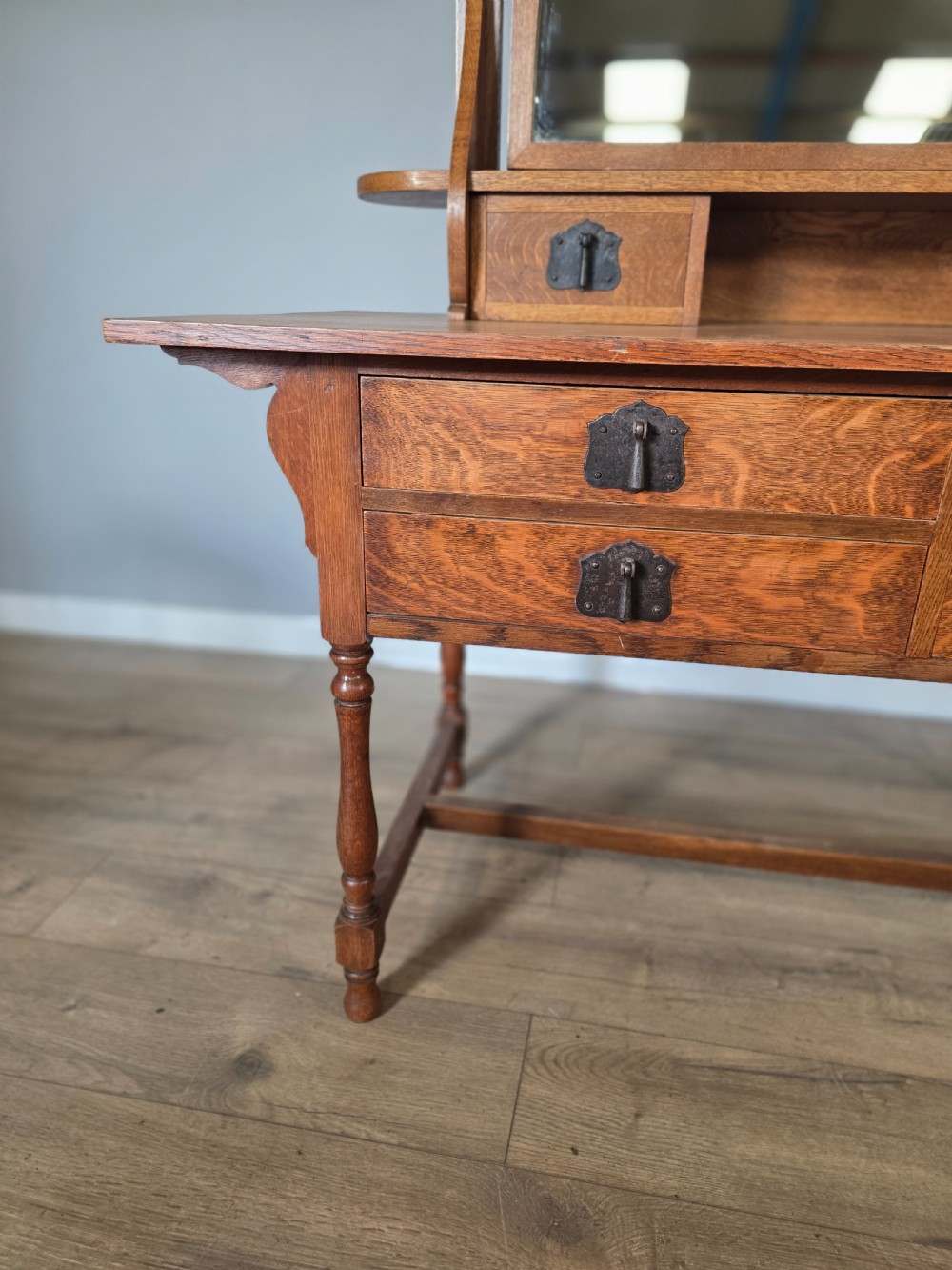 An Arts and Crafts solid oak dressing table featuring an upper mirror superstructure with side trinket drawers above a lower four-drawer chest with dark metal handles. View VII