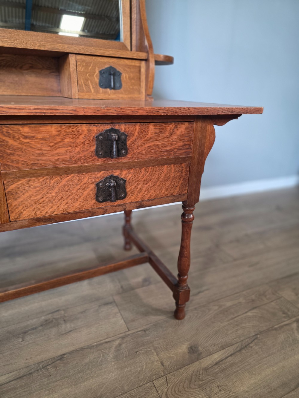 An Arts and Crafts solid oak dressing table featuring an upper mirror superstructure with side trinket drawers above a lower four-drawer chest with dark metal handles. View VIII