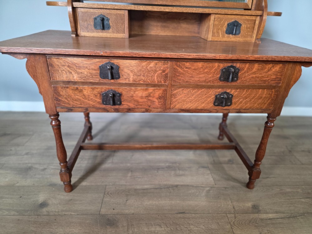 An Arts and Crafts solid oak dressing table featuring an upper mirror superstructure with side trinket drawers above a lower four-drawer chest with dark metal handles. View IX