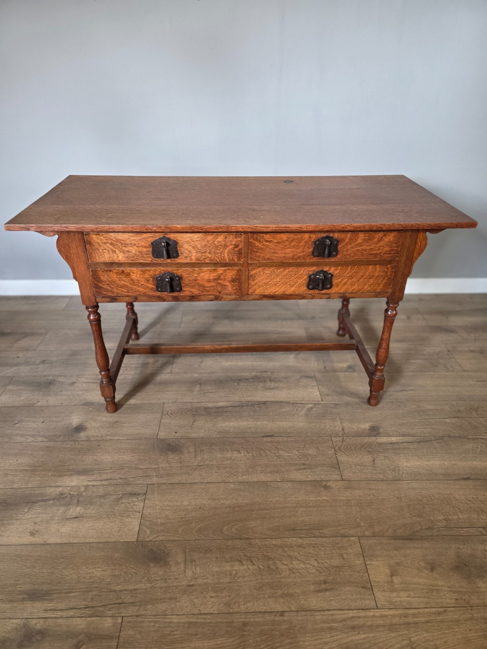 An Arts and Crafts solid oak dressing table featuring an upper mirror superstructure with side trinket drawers above a lower four-drawer chest with dark metal handles. View XVII