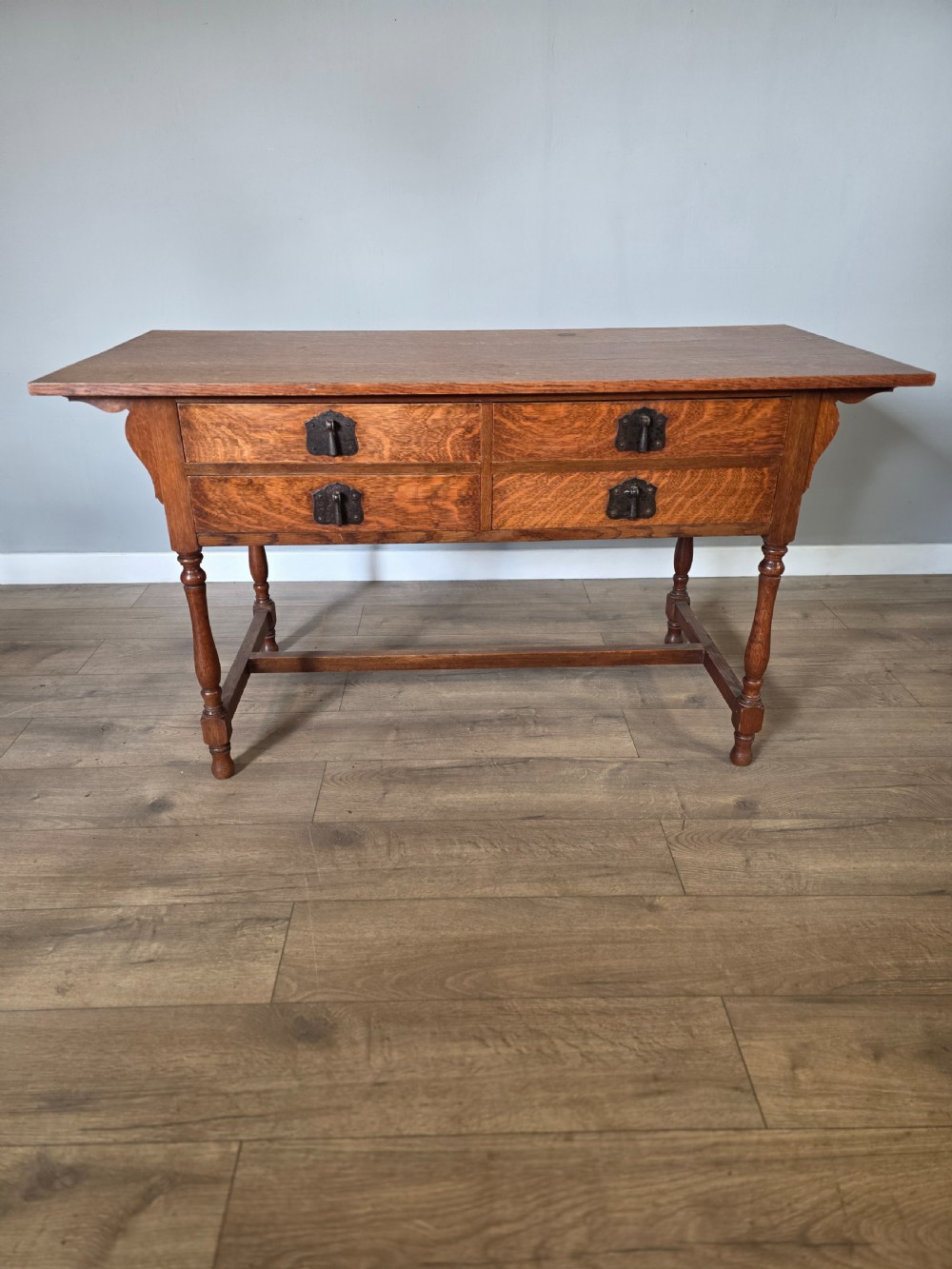 An Arts and Crafts solid oak dressing table featuring an upper mirror superstructure with side trinket drawers above a lower four-drawer chest with dark metal handles. View XVIII