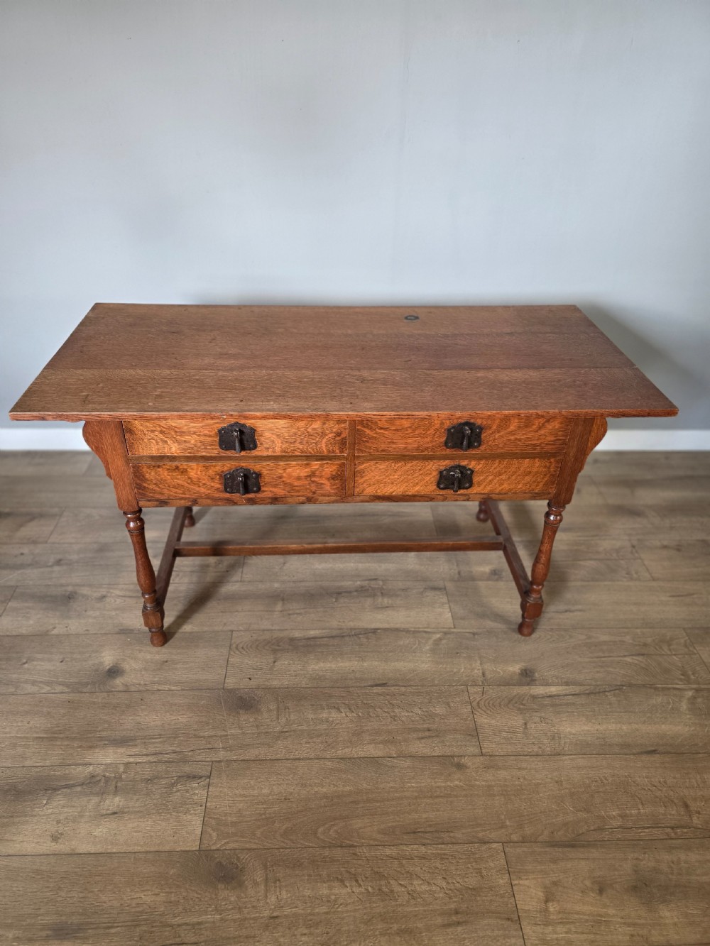 An Arts and Crafts solid oak dressing table featuring an upper mirror superstructure with side trinket drawers above a lower four-drawer chest with dark metal handles. View XIX