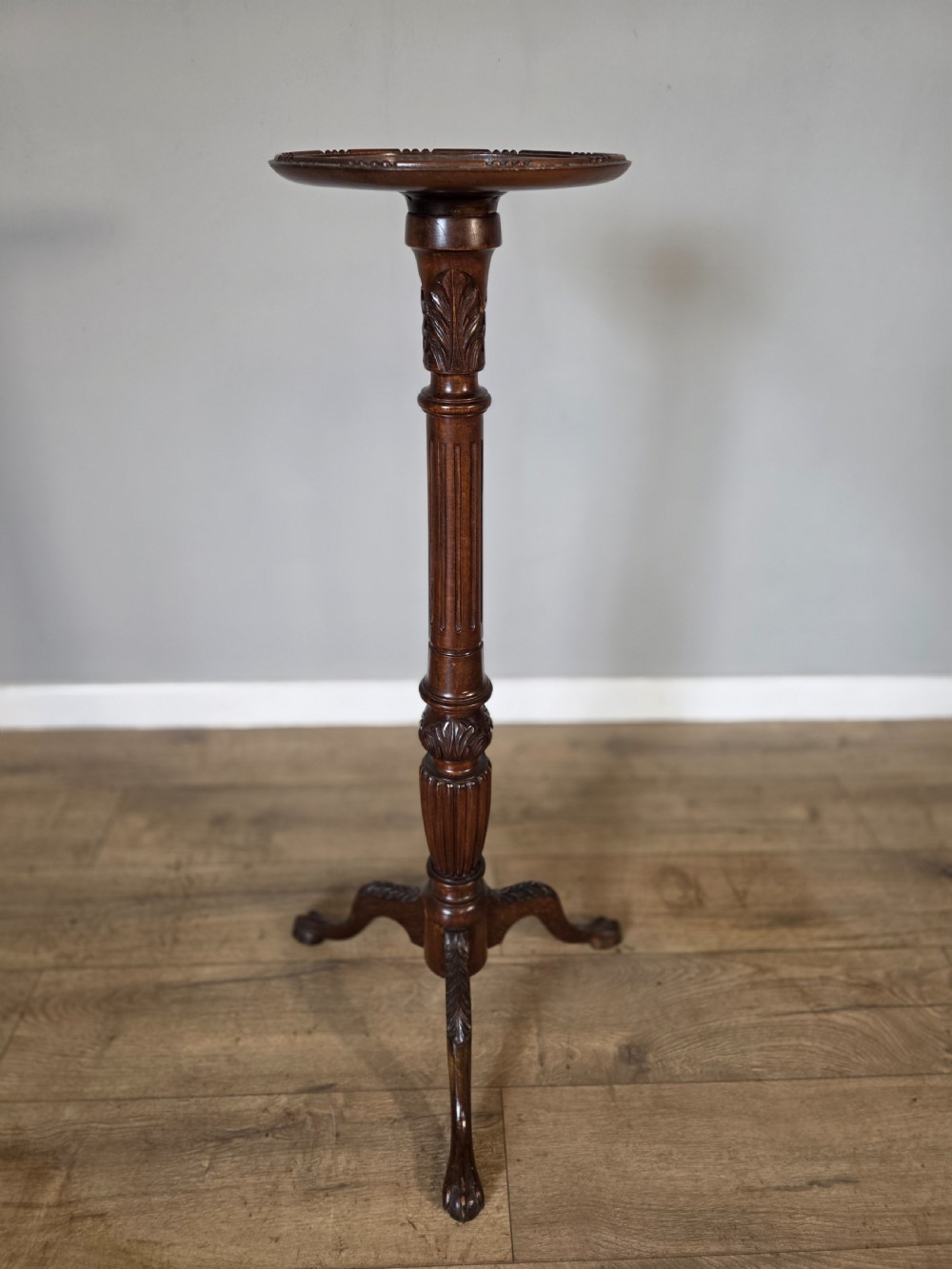 An antique dark mahogany Edwardian torchere plant stand with a circular top, fluted column, and tripod cabriole legs.