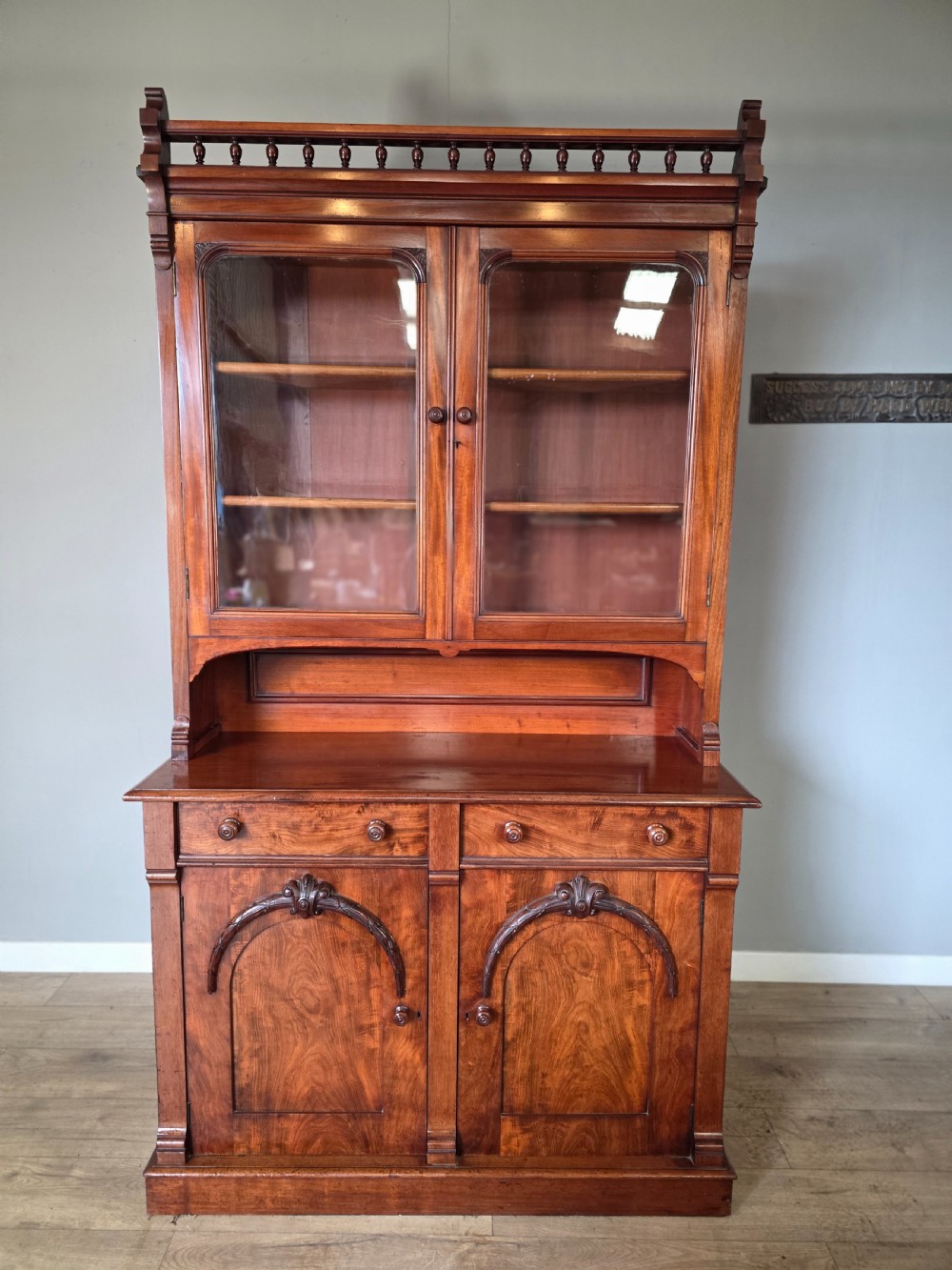 A Victorian mahogany glazed bookcase featuring a top spindle gallery, two glass cabinet doors, two drawers, and a lower double door cupboard on a plinth base.