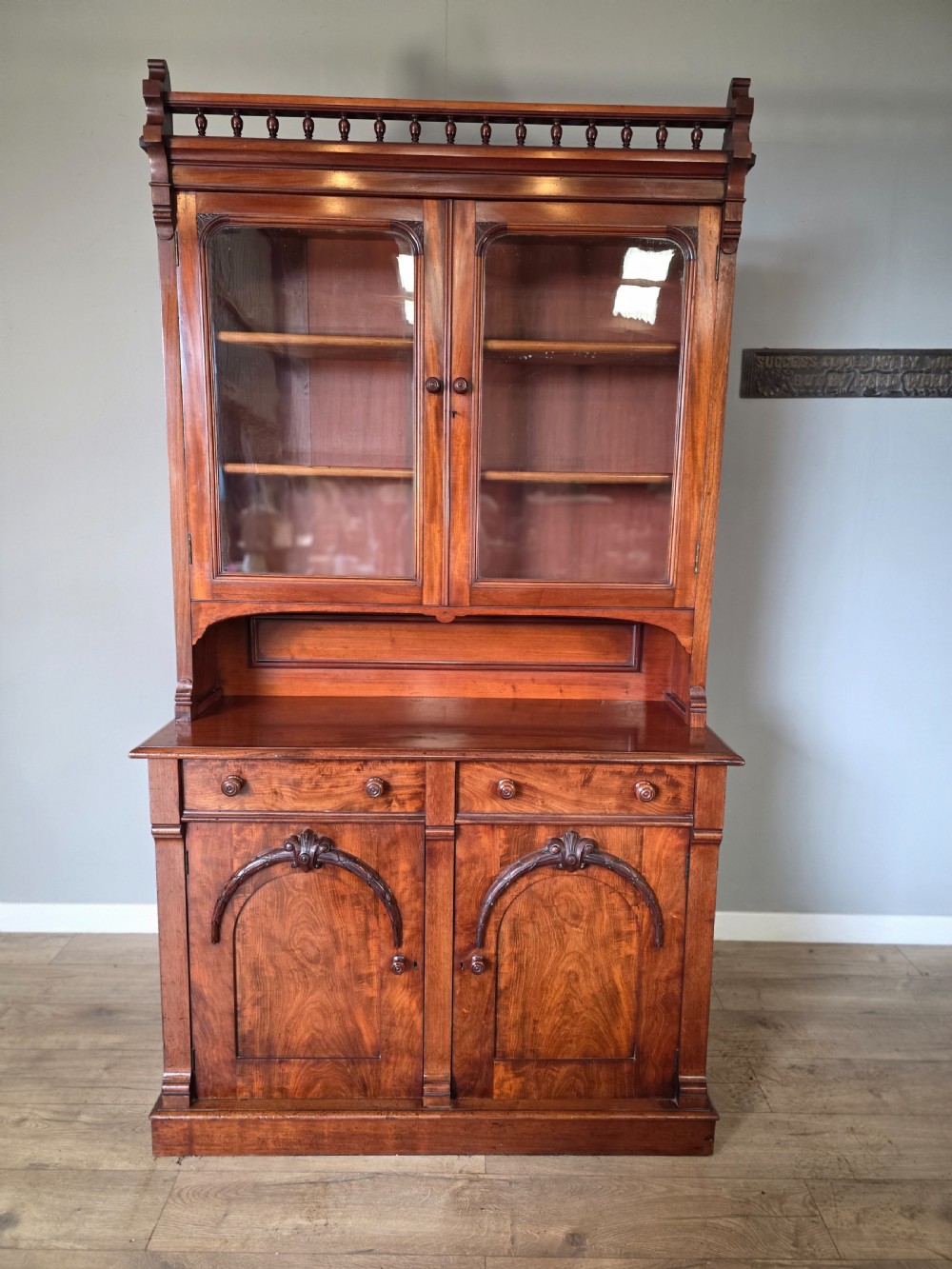 A Victorian mahogany glazed bookcase featuring a top spindle gallery, two glass cabinet doors, two drawers, and a lower double door cupboard on a plinth base. View II