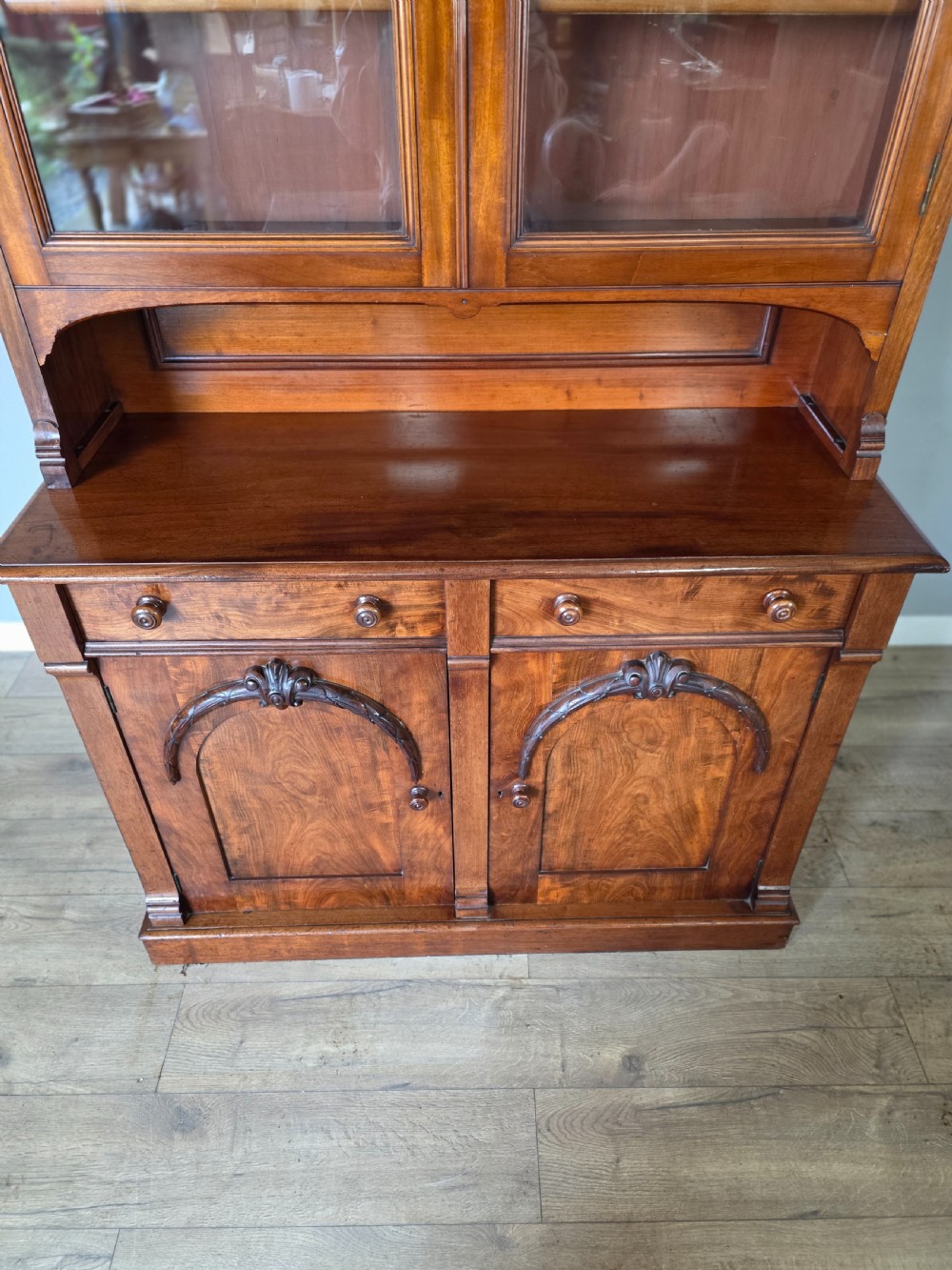 A Victorian mahogany glazed bookcase featuring a top spindle gallery, two glass cabinet doors, two drawers, and a lower double door cupboard on a plinth base. View IX