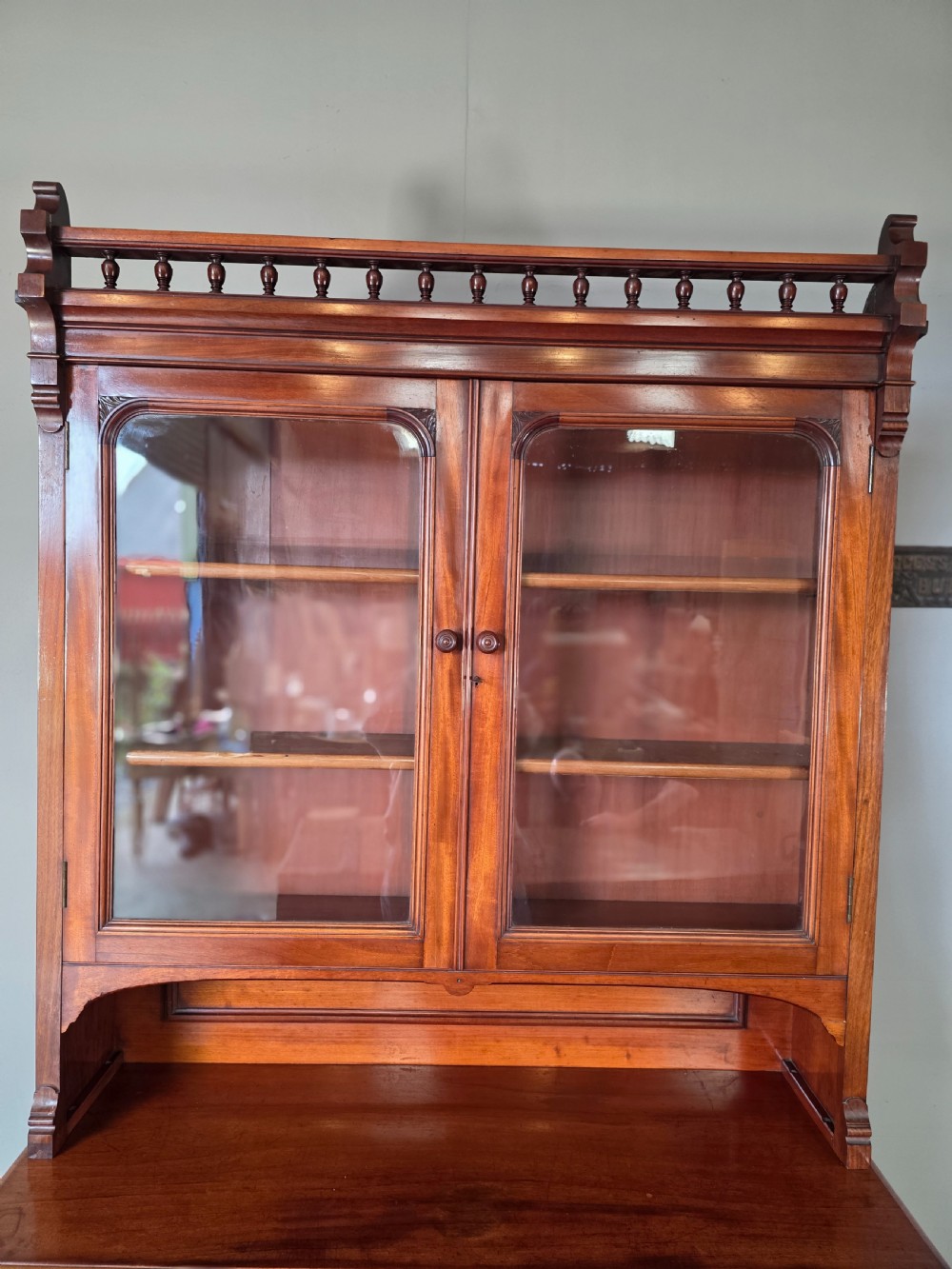 A Victorian mahogany glazed bookcase featuring a top spindle gallery, two glass cabinet doors, two drawers, and a lower double door cupboard on a plinth base. View X