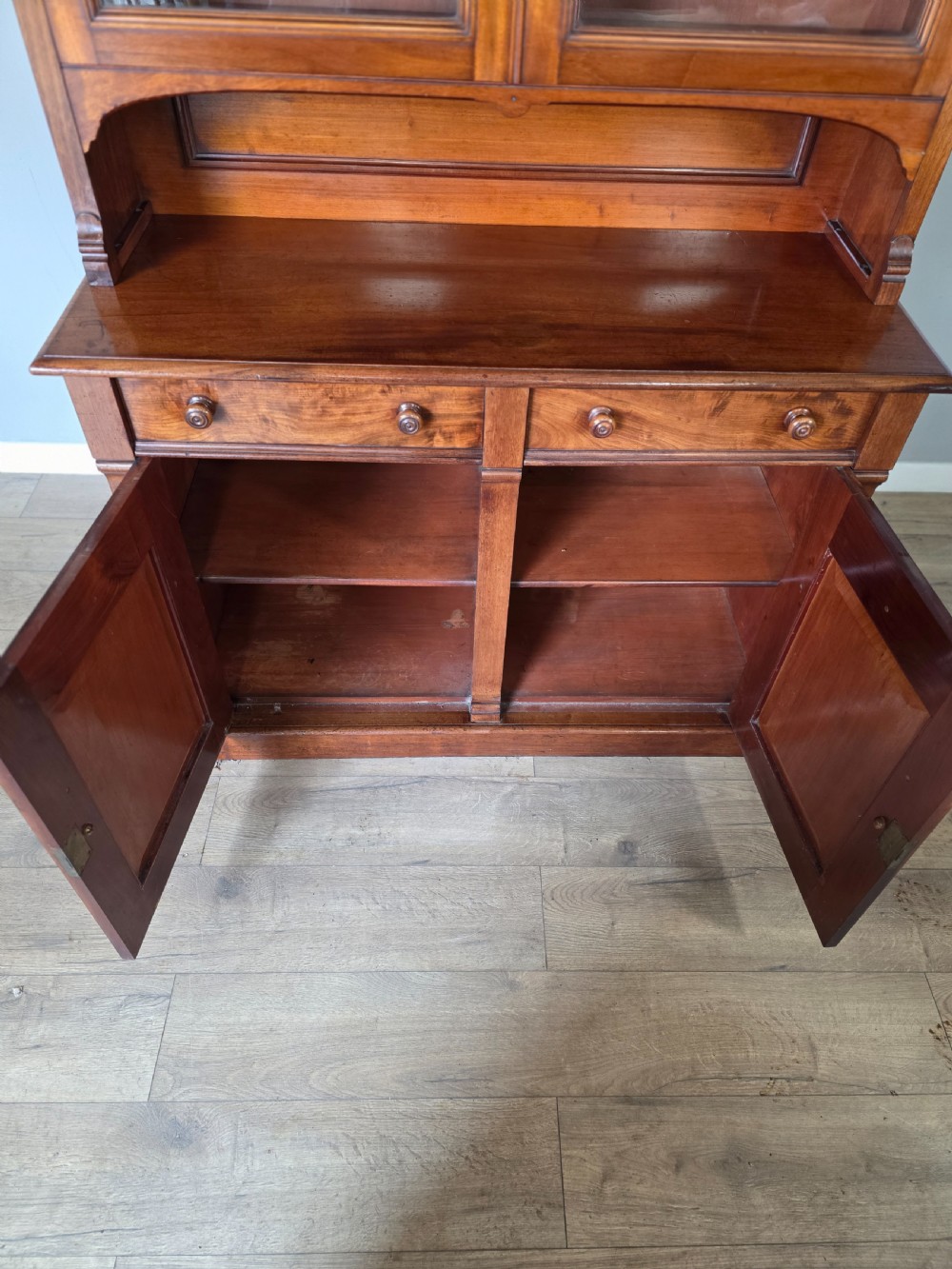 A Victorian mahogany glazed bookcase featuring a top spindle gallery, two glass cabinet doors, two drawers, and a lower double door cupboard on a plinth base. View XIII