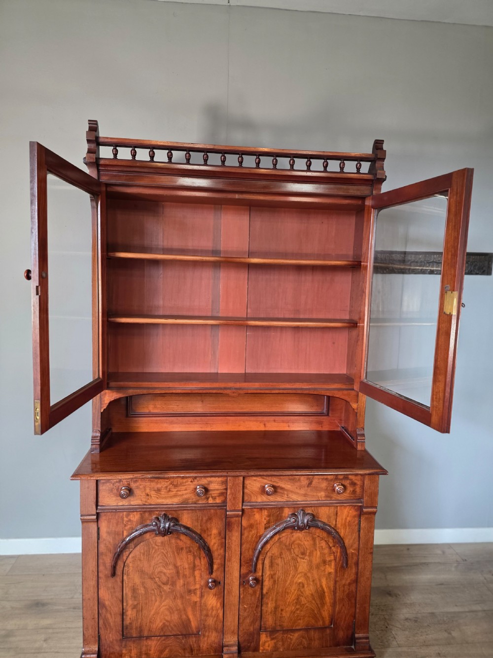 A Victorian mahogany glazed bookcase featuring a top spindle gallery, two glass cabinet doors, two drawers, and a lower double door cupboard on a plinth base. View XIV