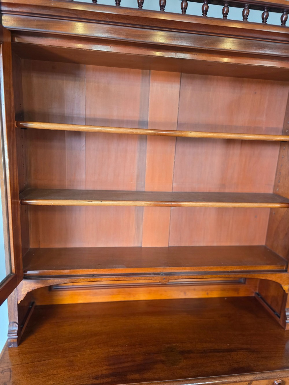 A Victorian mahogany glazed bookcase featuring a top spindle gallery, two glass cabinet doors, two drawers, and a lower double door cupboard on a plinth base. View XVI