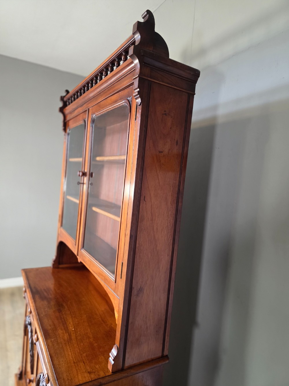 A Victorian mahogany glazed bookcase featuring a top spindle gallery, two glass cabinet doors, two drawers, and a lower double door cupboard on a plinth base. View XIX