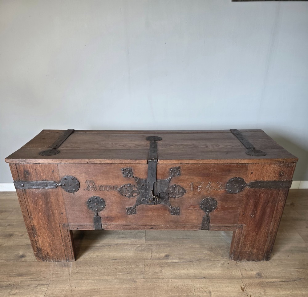An 18th-century oak coffer featuring hand-forged wrought iron straps, a central escutcheon plate, and the carved inscription Anno 1743 on the front panel.