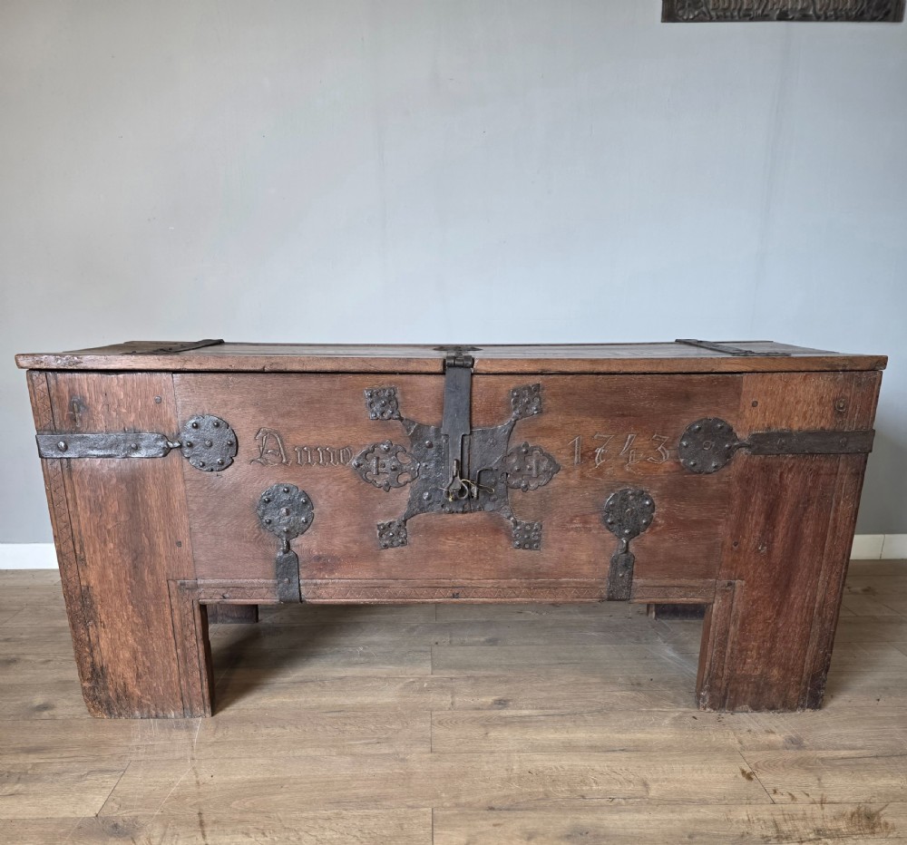 An 18th-century oak coffer featuring hand-forged wrought iron straps, a central escutcheon plate, and the carved inscription Anno 1743 on the front panel. View II