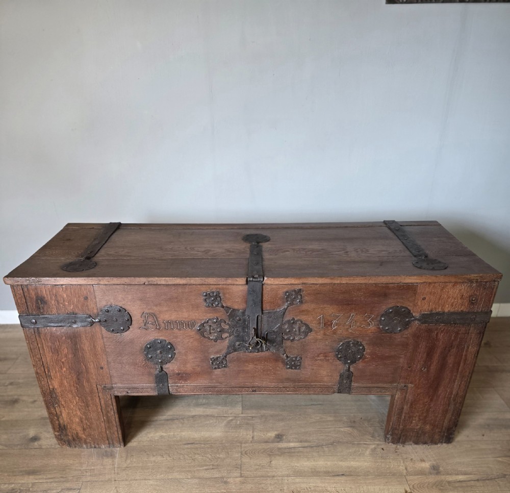 An 18th-century oak coffer featuring hand-forged wrought iron straps, a central escutcheon plate, and the carved inscription Anno 1743 on the front panel. View III