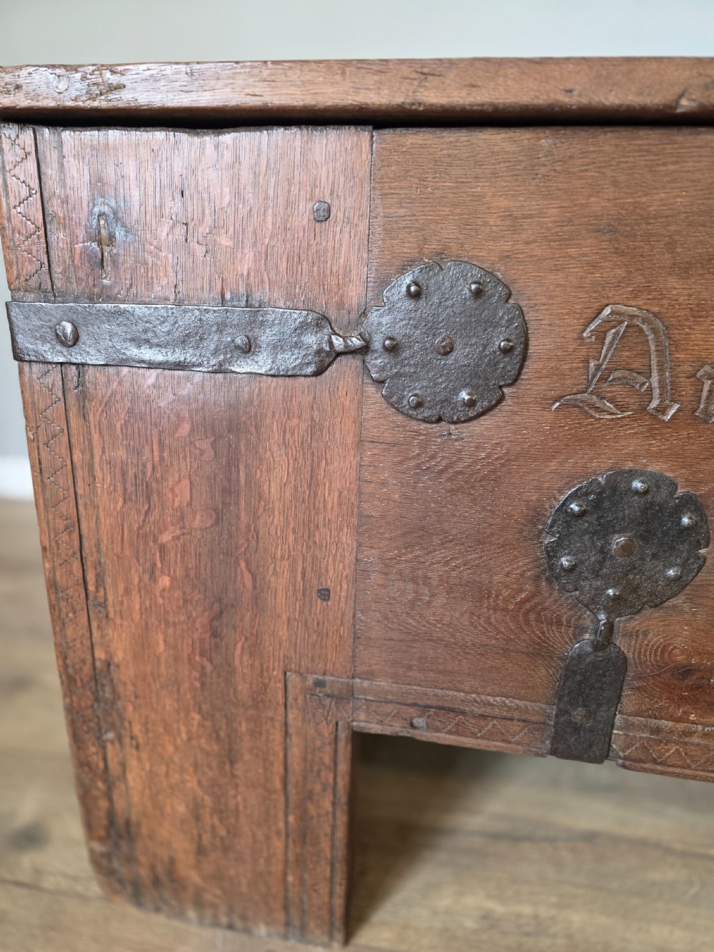 An 18th-century oak coffer featuring hand-forged wrought iron straps, a central escutcheon plate, and the carved inscription Anno 1743 on the front panel. View V