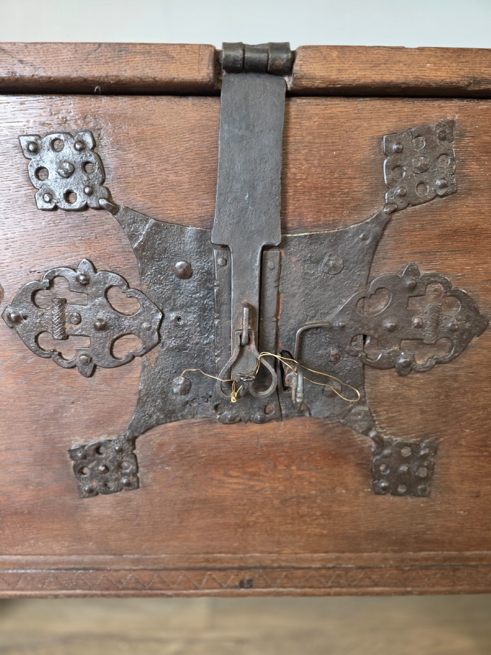 An 18th-century oak coffer featuring hand-forged wrought iron straps, a central escutcheon plate, and the carved inscription Anno 1743 on the front panel. View VII
