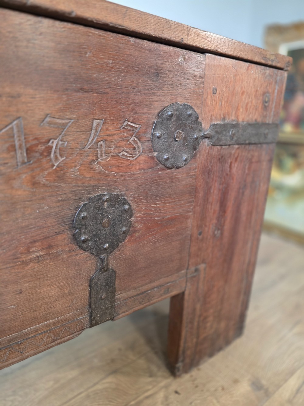 An 18th-century oak coffer featuring hand-forged wrought iron straps, a central escutcheon plate, and the carved inscription Anno 1743 on the front panel. View VIII