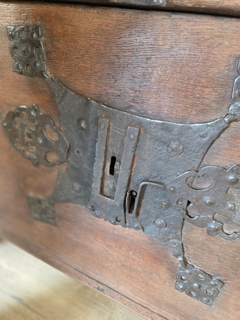 An 18th-century oak coffer featuring hand-forged wrought iron straps, a central escutcheon plate, and the carved inscription Anno 1743 on the front panel. View XII