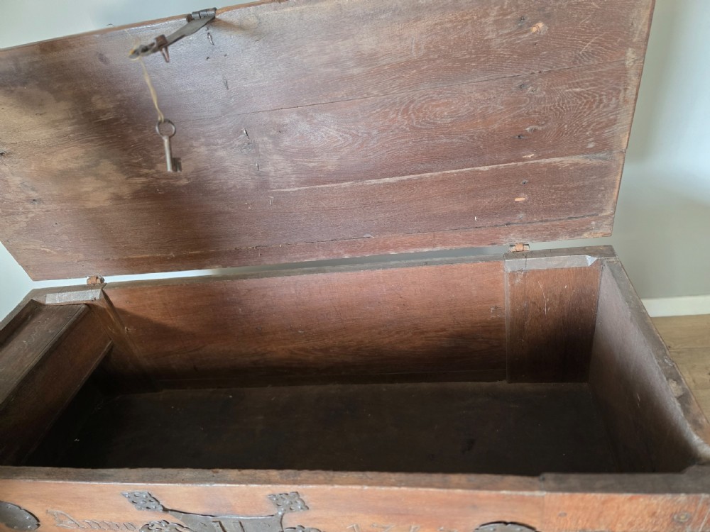 An 18th-century oak coffer featuring hand-forged wrought iron straps, a central escutcheon plate, and the carved inscription Anno 1743 on the front panel. View XIII