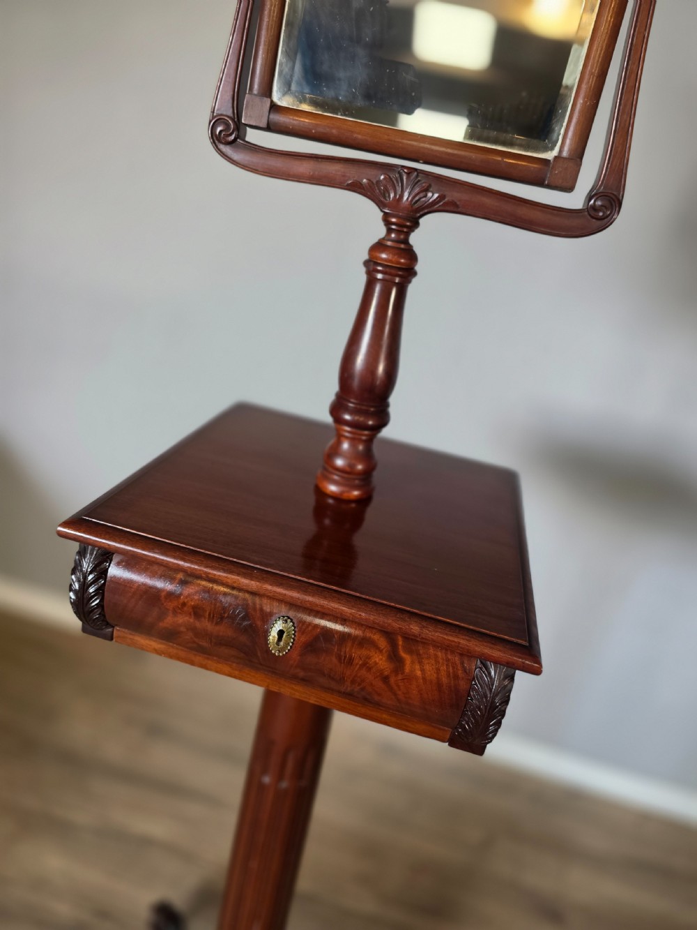 A tall mahogany gentlemans shaving stand featuring an adjustable rectangular mirror, a single drawer pedestal, a fluted column, and a carved tripod base. View V