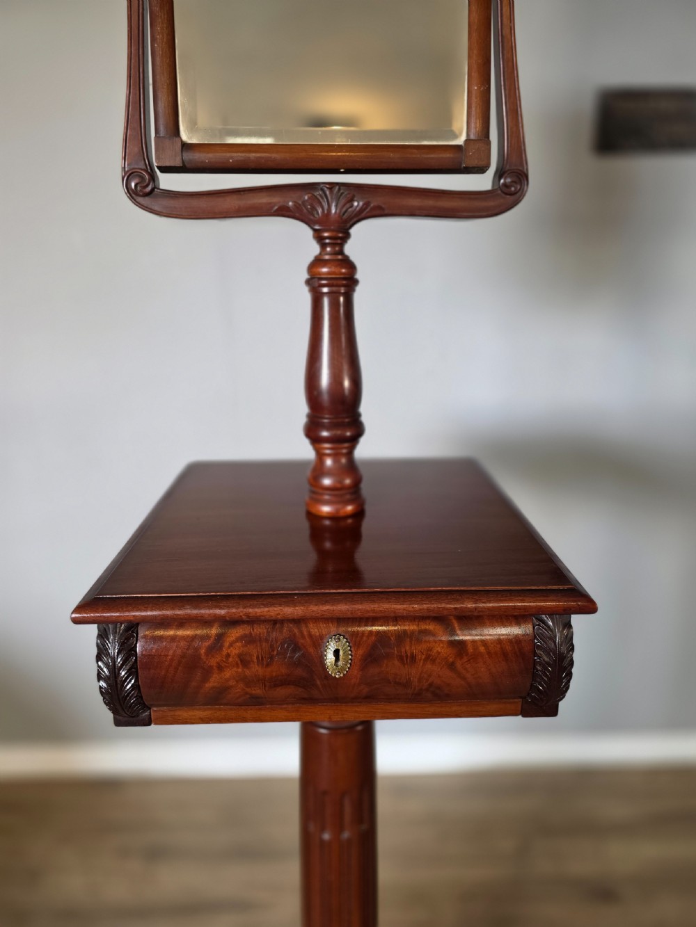 A tall mahogany gentlemans shaving stand featuring an adjustable rectangular mirror, a single drawer pedestal, a fluted column, and a carved tripod base. View X
