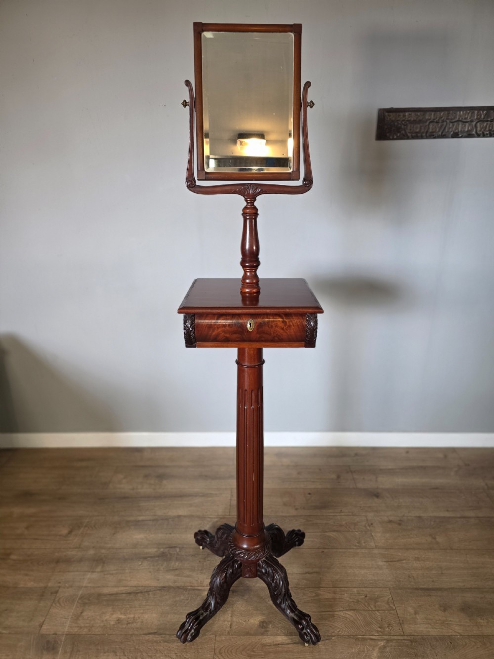 A tall mahogany gentlemans shaving stand featuring an adjustable rectangular mirror, a single drawer pedestal, a fluted column, and a carved tripod base. View XVI
