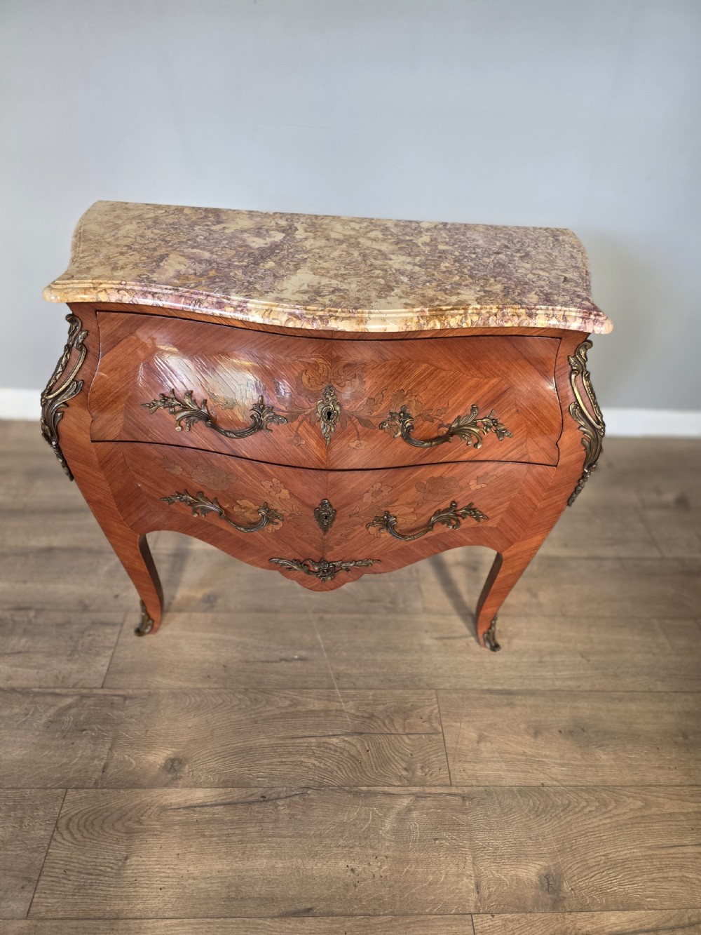 A French Rococo style bombe commode featuring a shaped marble top, floral marquetry veneer, two drawers, and ornamental gilt bronze mounts. View III