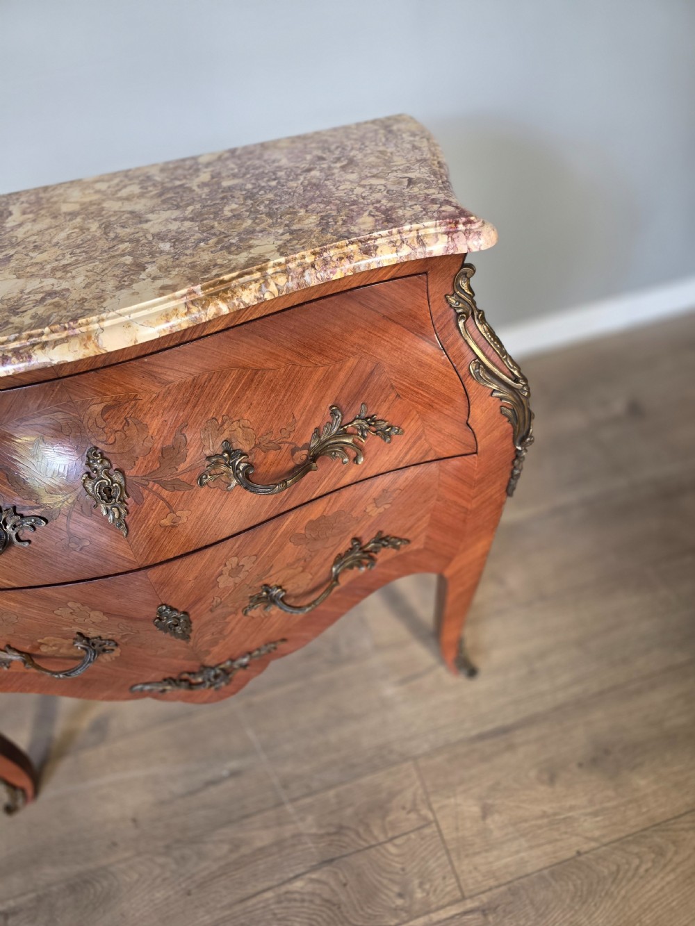 A French Rococo style bombe commode featuring a shaped marble top, floral marquetry veneer, two drawers, and ornamental gilt bronze mounts. View VI