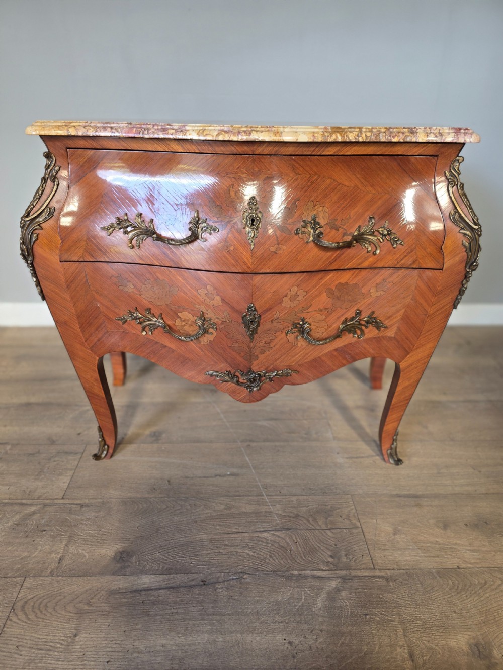 A French Rococo style bombe commode featuring a shaped marble top, floral marquetry veneer, two drawers, and ornamental gilt bronze mounts. View VIII
