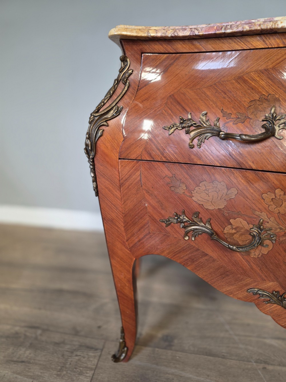 A French Rococo style bombe commode featuring a shaped marble top, floral marquetry veneer, two drawers, and ornamental gilt bronze mounts. View IX