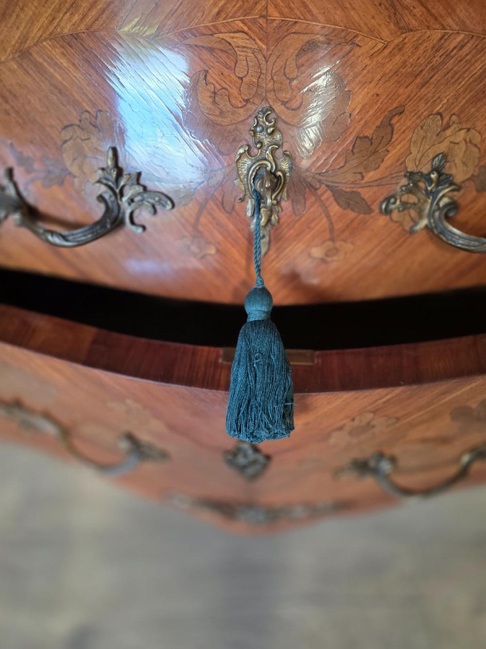A French Rococo style bombe commode featuring a shaped marble top, floral marquetry veneer, two drawers, and ornamental gilt bronze mounts. View XI
