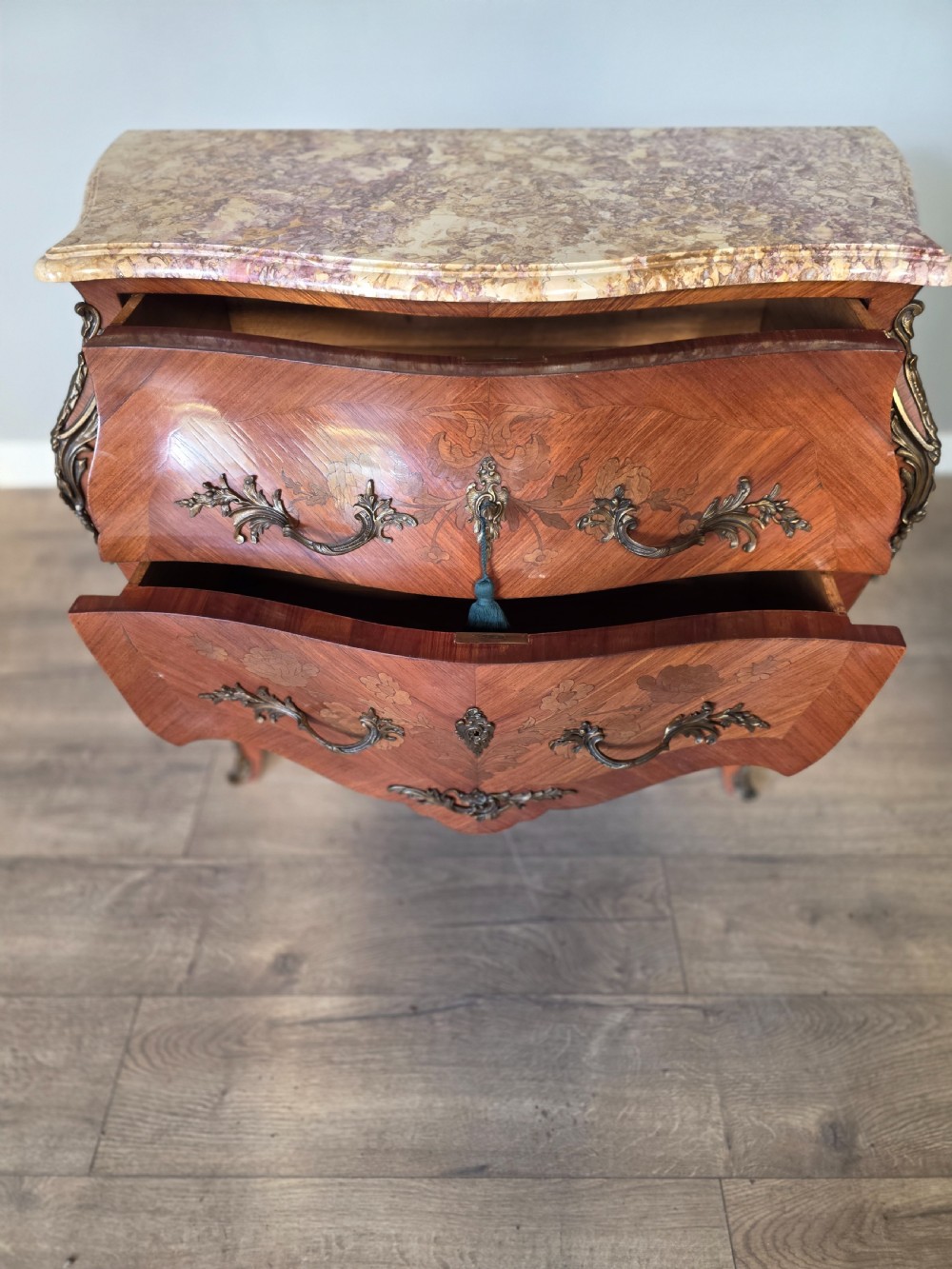 A French Rococo style bombe commode featuring a shaped marble top, floral marquetry veneer, two drawers, and ornamental gilt bronze mounts. View XII