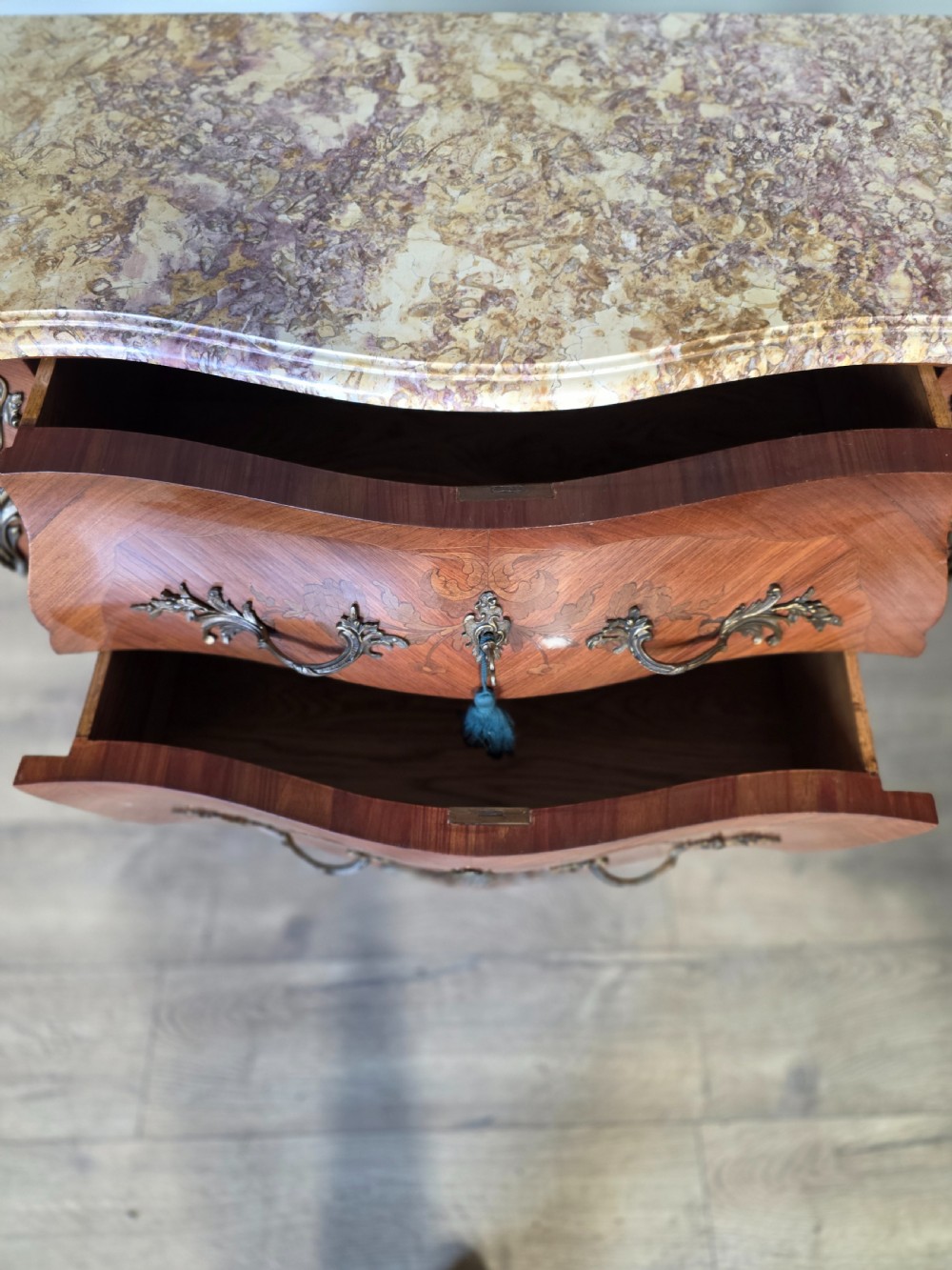 A French Rococo style bombe commode featuring a shaped marble top, floral marquetry veneer, two drawers, and ornamental gilt bronze mounts. View XIII