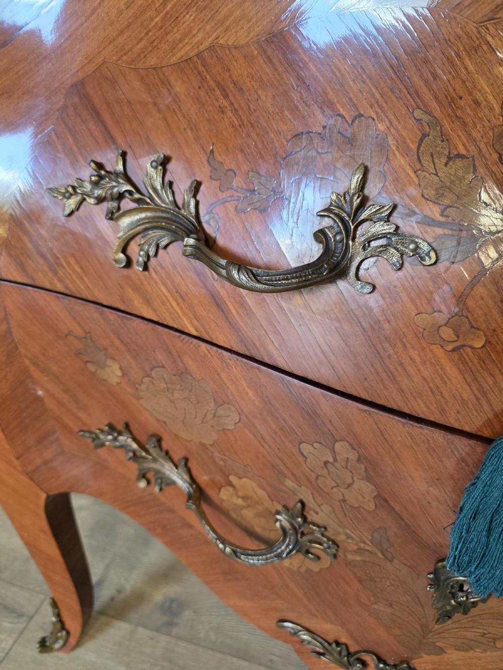 A French Rococo style bombe commode featuring a shaped marble top, floral marquetry veneer, two drawers, and ornamental gilt bronze mounts. View XIX