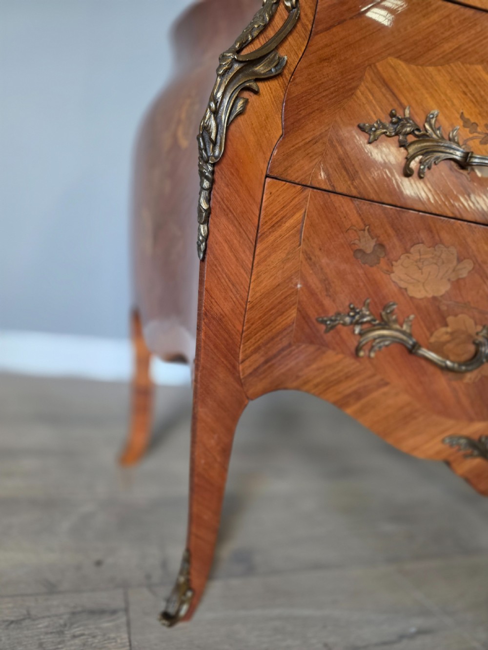 A French Rococo style bombe commode featuring a shaped marble top, floral marquetry veneer, two drawers, and ornamental gilt bronze mounts. View XXI
