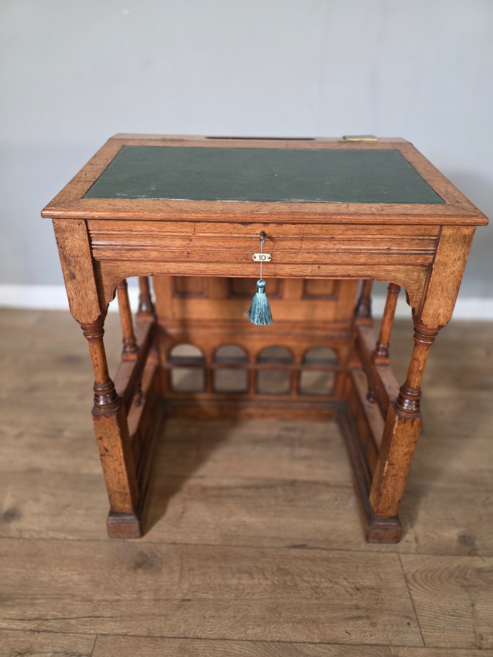 A late Victorian oak clerks desk with an inset green leather writing top, turned legs, and an arcaded lower framework.