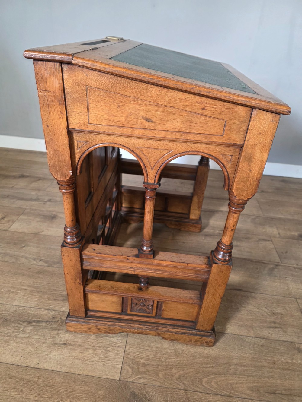 A late Victorian oak clerks desk with an inset green leather writing top, turned legs, and an arcaded lower framework. View XV