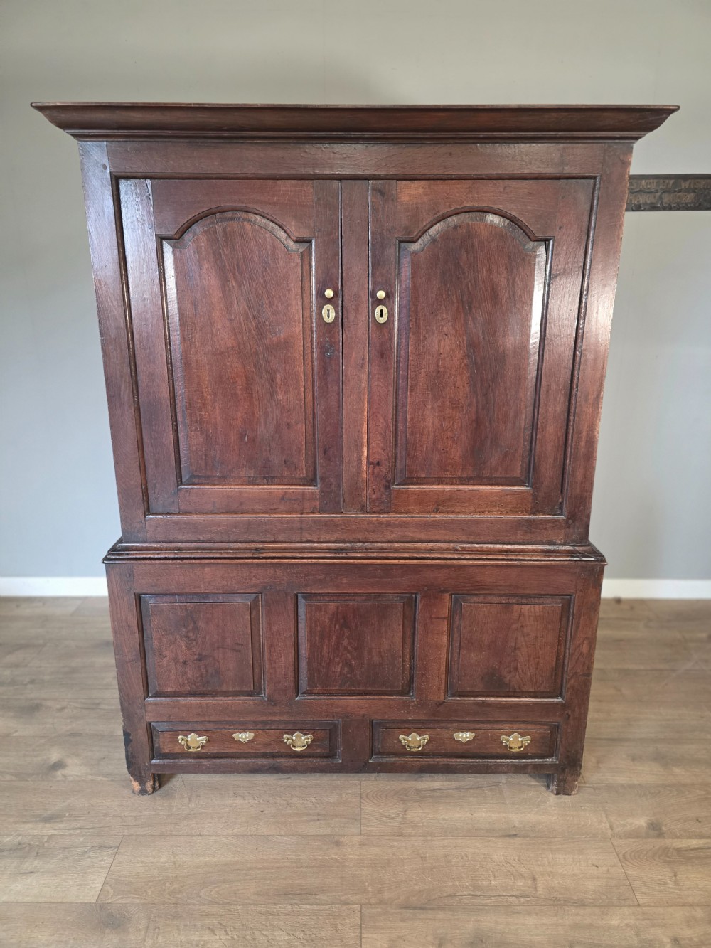 A dark oak two-tier antique cupboard with arched panel double doors above a base with recessed panels and two drawers.