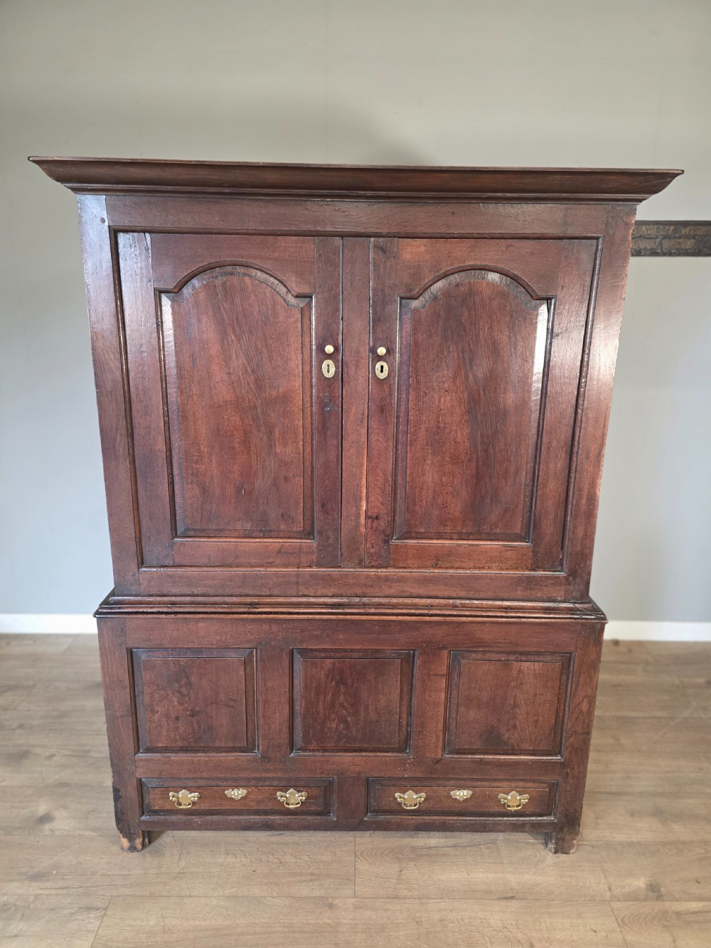 A dark oak two-tier antique cupboard with arched panel double doors above a base with recessed panels and two drawers. View II