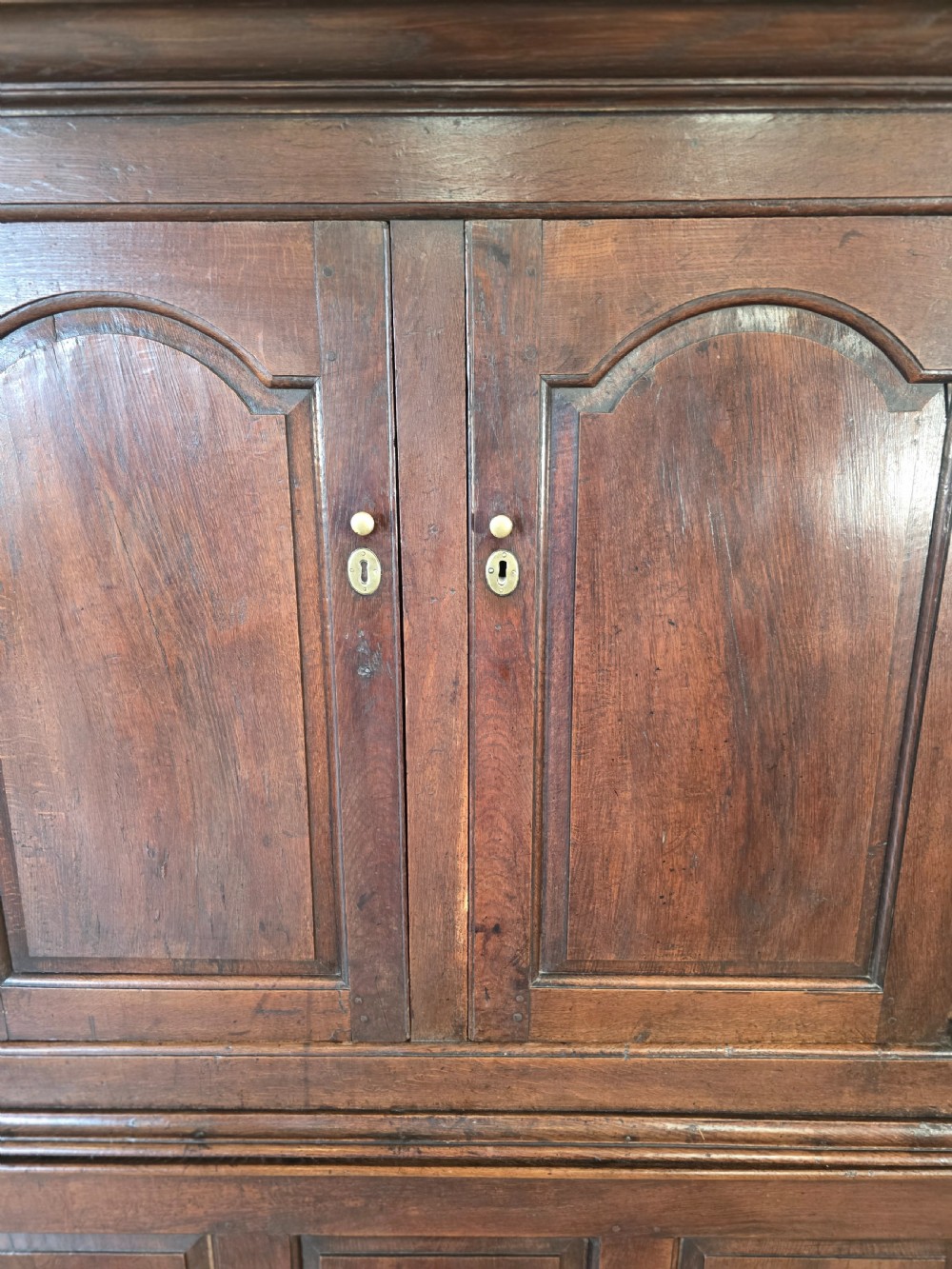 A dark oak two-tier antique cupboard with arched panel double doors above a base with recessed panels and two drawers. View III