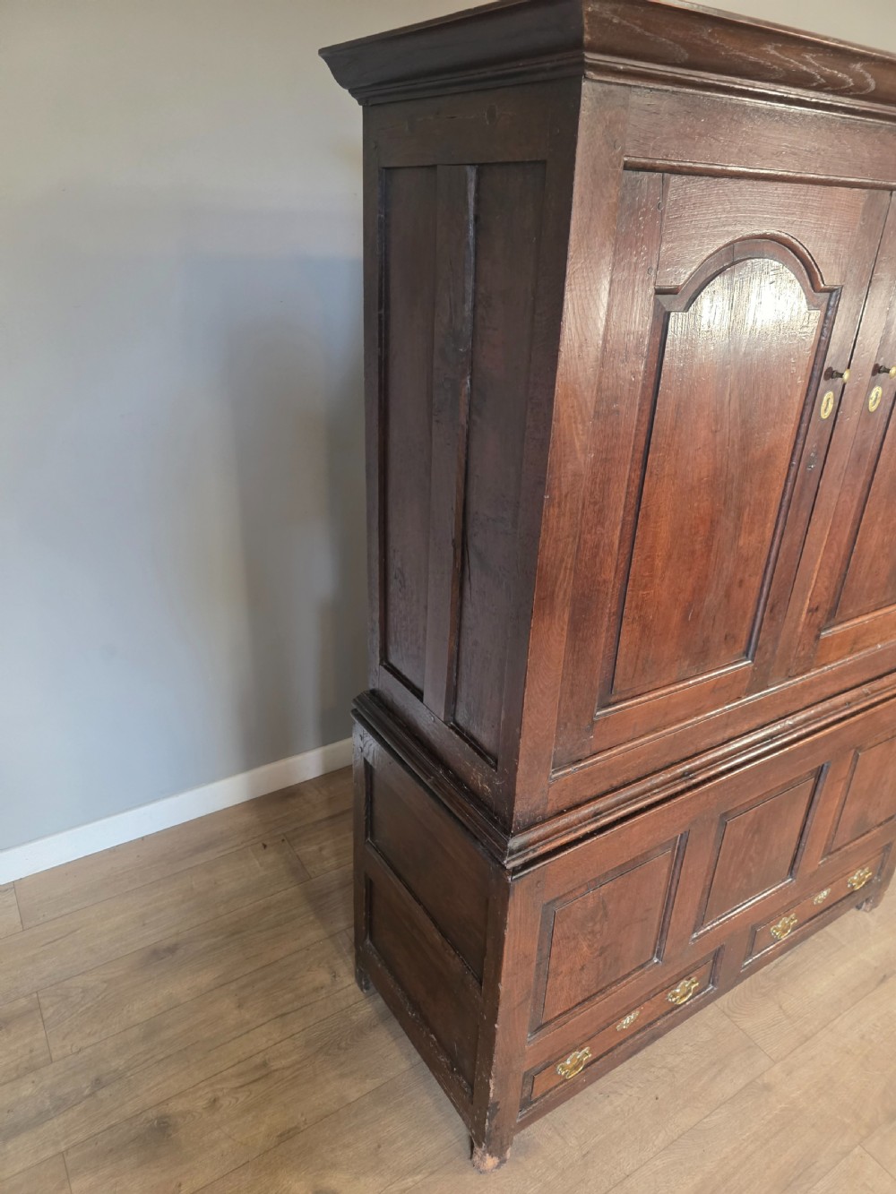 A dark oak two-tier antique cupboard with arched panel double doors above a base with recessed panels and two drawers. View VI