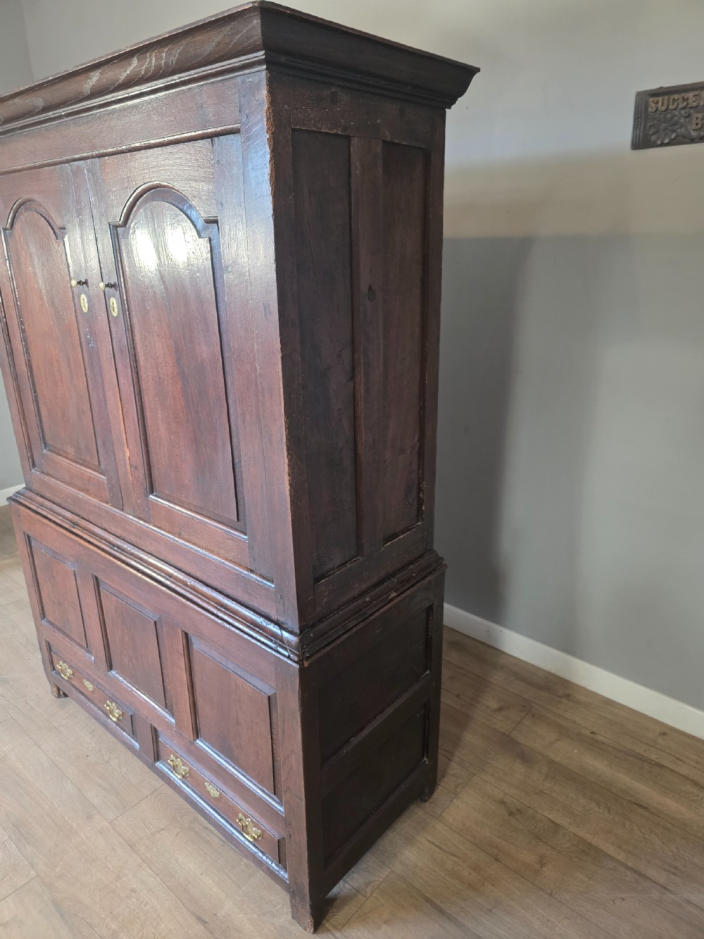 A dark oak two-tier antique cupboard with arched panel double doors above a base with recessed panels and two drawers. View VII