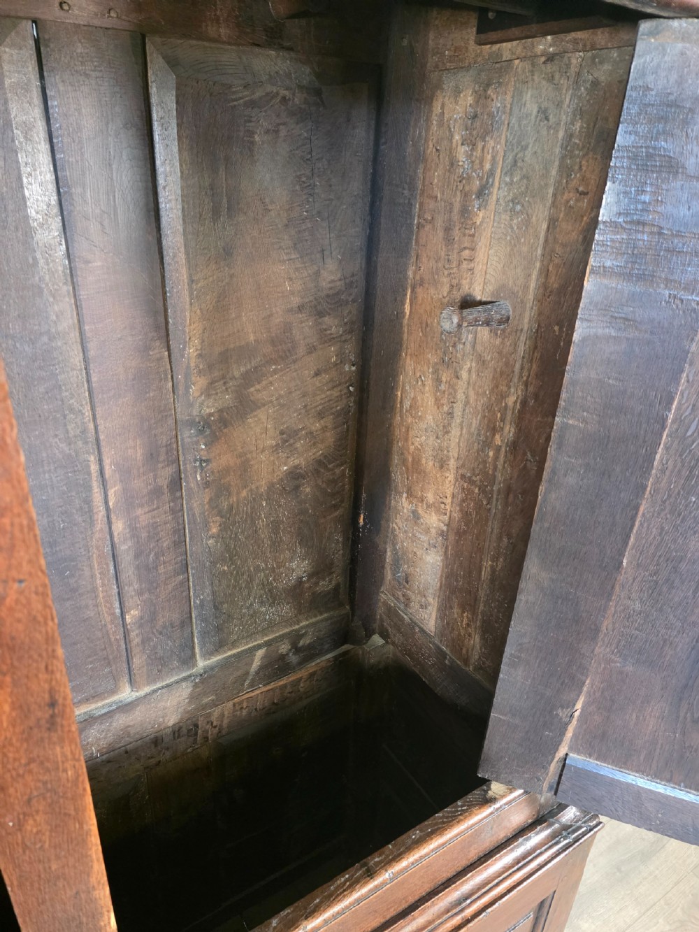 A dark oak two-tier antique cupboard with arched panel double doors above a base with recessed panels and two drawers. View X