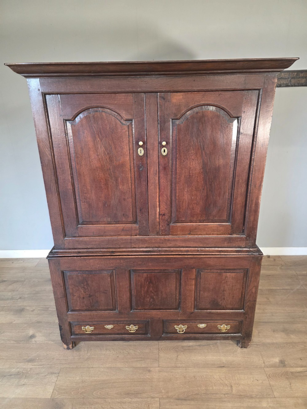 A dark oak two-tier antique cupboard with arched panel double doors above a base with recessed panels and two drawers. View XI
