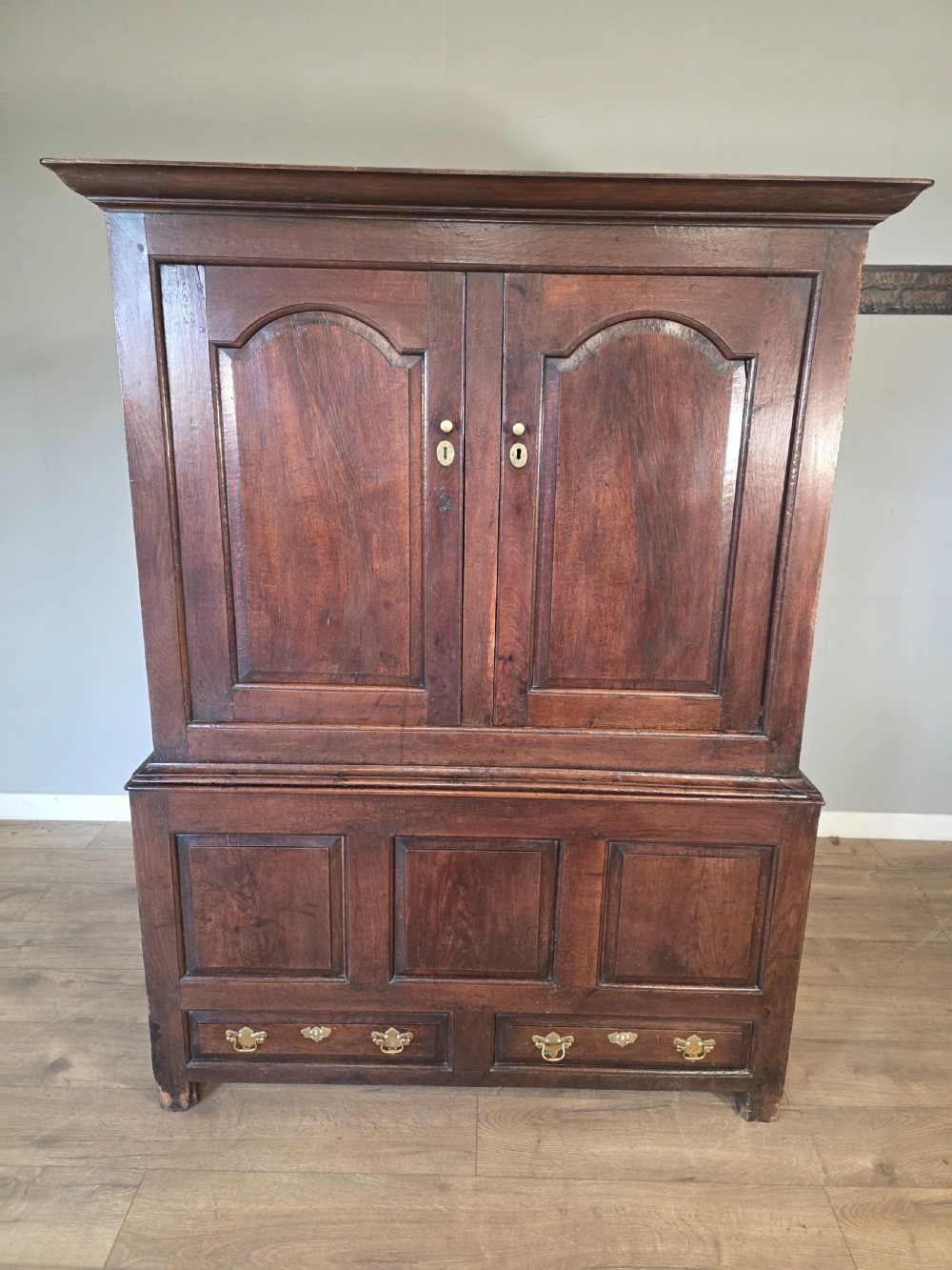 A dark oak two-tier antique cupboard with arched panel double doors above a base with recessed panels and two drawers. View XX
