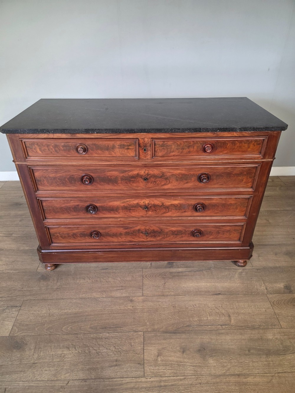 A nineteenth-century French mahogany chest of drawers featuring a dark marble top, flame mahogany drawer fronts, turned wooden knobs, and a plinth base.